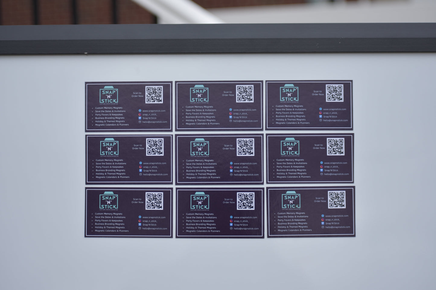 Nine custom magnetic business cards displayed on a metal surface — bulk magnetic business card order by Snap'N'Stick
